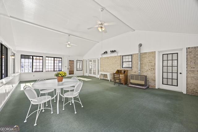 interior space with brick wall, ceiling fan, high vaulted ceiling, carpet floors, and a wood stove