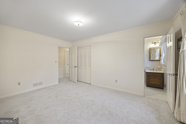 unfurnished bedroom with sink, ensuite bathroom, light colored carpet, a closet, and ornamental molding