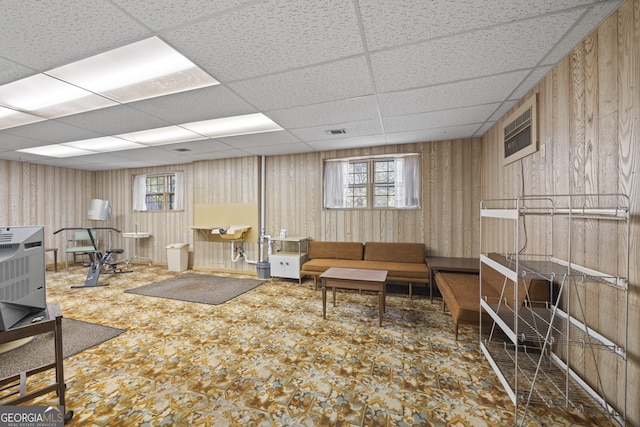 living room with a paneled ceiling, wood walls, and heating unit