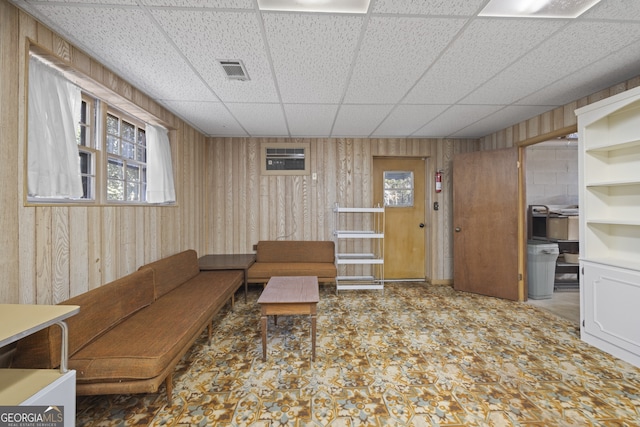 living room with a drop ceiling, wooden walls, and built in shelves