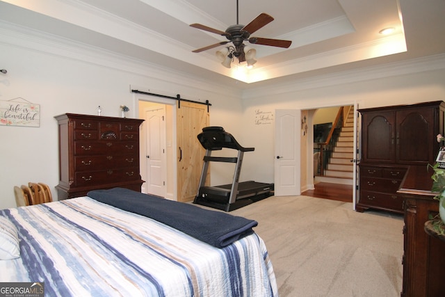 carpeted bedroom with a barn door, a tray ceiling, ceiling fan, and crown molding