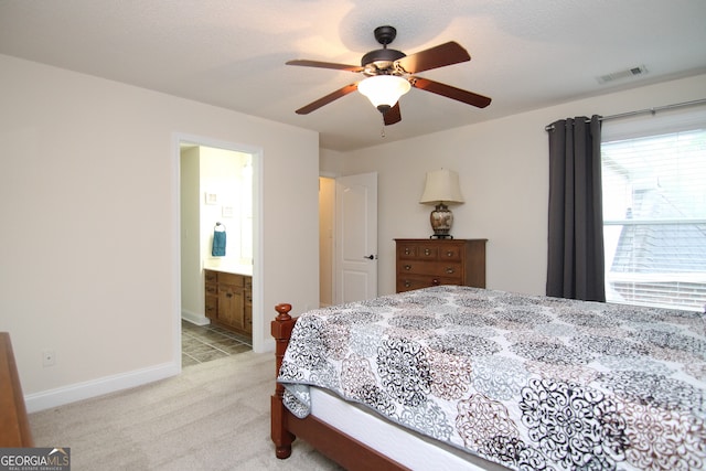 bedroom with a textured ceiling, light colored carpet, ensuite bath, and ceiling fan