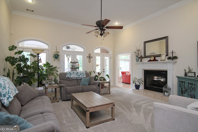 living room with french doors, light colored carpet, ceiling fan, crown molding, and a tile fireplace