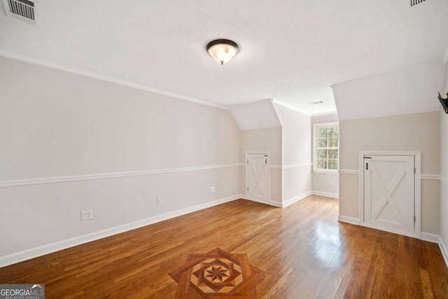 additional living space with a textured ceiling, lofted ceiling, and hardwood / wood-style flooring