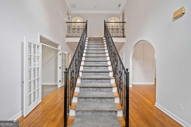 staircase with crown molding, french doors, a towering ceiling, and hardwood / wood-style flooring