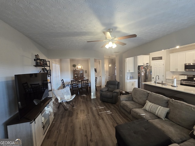 living room with a textured ceiling, ceiling fan, dark wood-type flooring, and sink