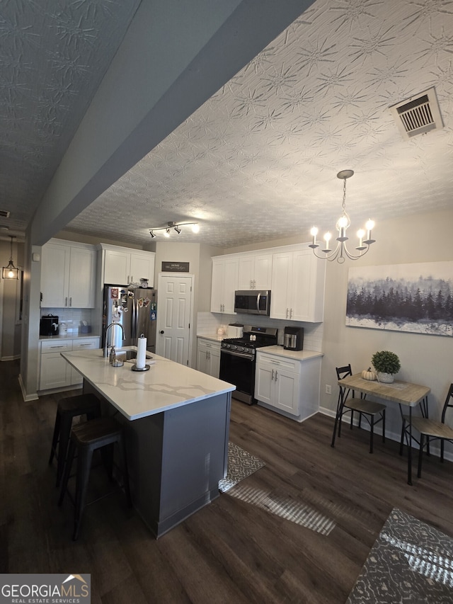 kitchen featuring appliances with stainless steel finishes, a textured ceiling, a kitchen island with sink, pendant lighting, and white cabinetry