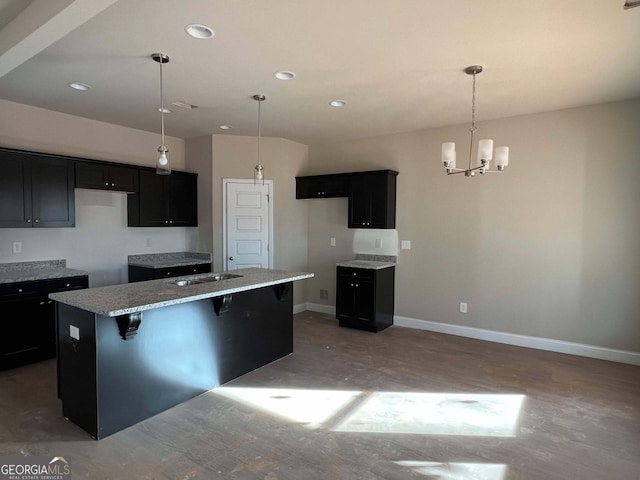 kitchen with hanging light fixtures, light stone counters, a chandelier, a kitchen island with sink, and a kitchen bar