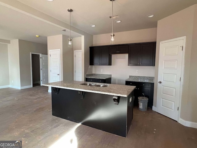 kitchen with hardwood / wood-style floors, a breakfast bar, pendant lighting, an island with sink, and light stone countertops