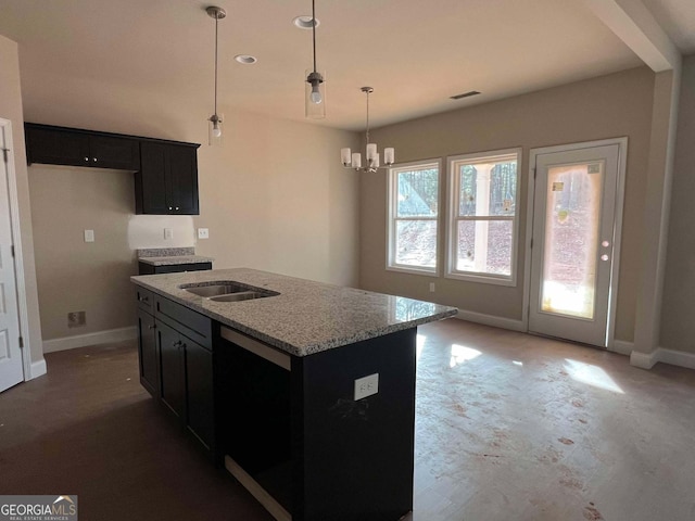 kitchen with a kitchen island with sink, hanging light fixtures, black dishwasher, sink, and light stone counters