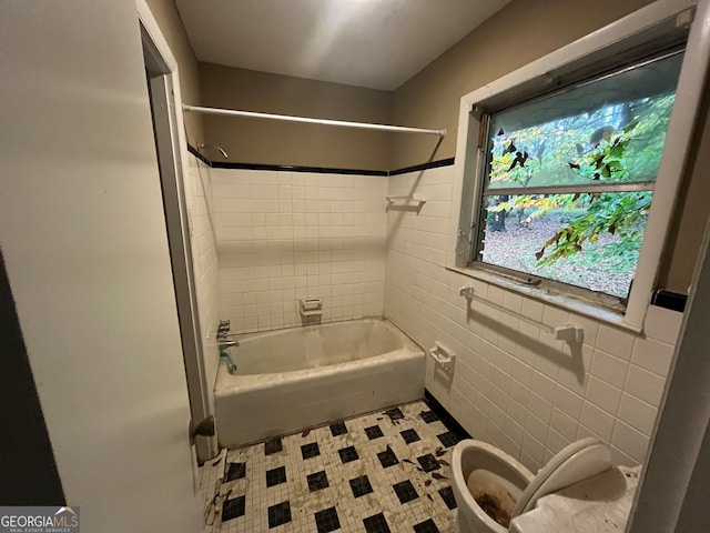 bathroom with tile patterned flooring, tiled shower / bath combo, tile walls, and toilet