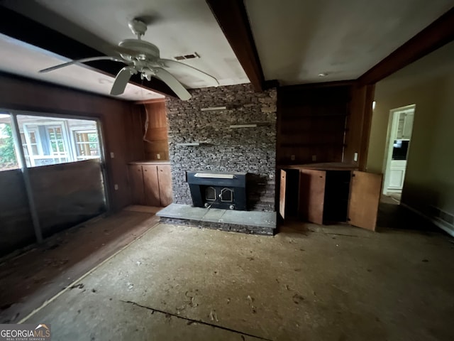 unfurnished living room with beamed ceiling, a wood stove, and ceiling fan