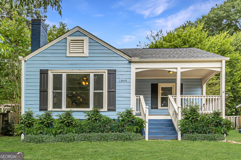 bungalow with a porch, a front yard, a shingled roof, and a chimney