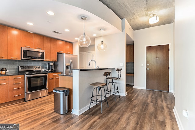 kitchen featuring dark hardwood / wood-style flooring, backsplash, pendant lighting, a breakfast bar area, and appliances with stainless steel finishes