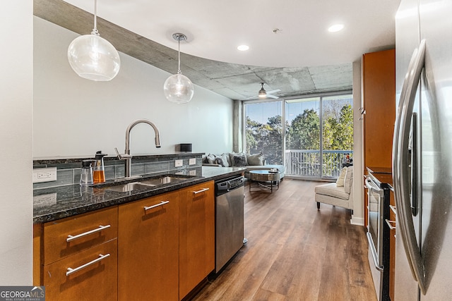 kitchen with appliances with stainless steel finishes, sink, pendant lighting, hardwood / wood-style flooring, and dark stone countertops