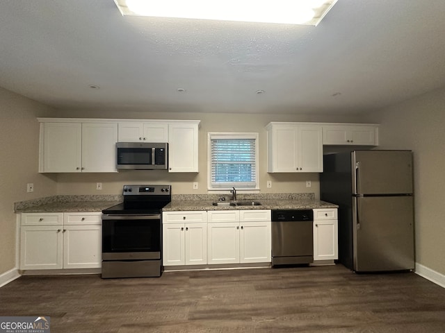 kitchen with white cabinetry, sink, light stone counters, dark hardwood / wood-style floors, and appliances with stainless steel finishes