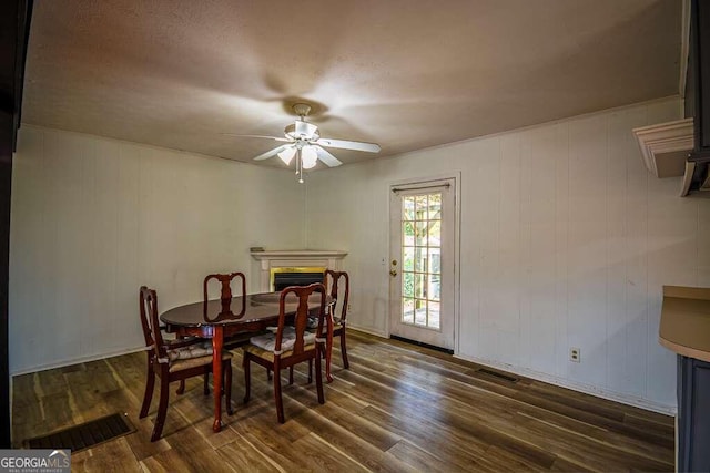 dining space with a textured ceiling, ceiling fan, wood walls, and dark wood-type flooring