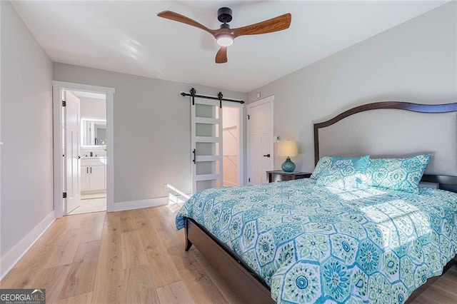 bedroom with a barn door, ensuite bathroom, light hardwood / wood-style flooring, and ceiling fan