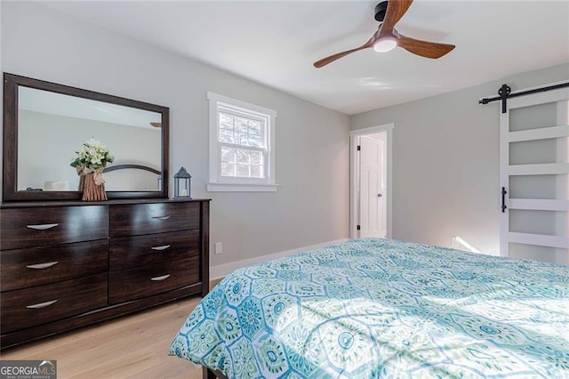 bedroom featuring a barn door, ceiling fan, and light wood-type flooring