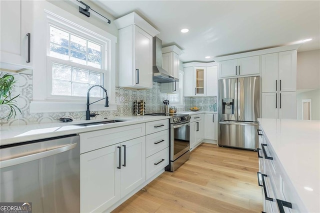 kitchen with decorative backsplash, appliances with stainless steel finishes, wall chimney exhaust hood, sink, and white cabinets