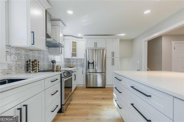 kitchen with backsplash, stainless steel appliances, wall chimney range hood, light hardwood / wood-style floors, and white cabinetry