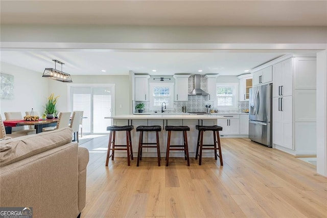 kitchen featuring a kitchen breakfast bar, stainless steel refrigerator with ice dispenser, wall chimney exhaust hood, tasteful backsplash, and white cabinetry