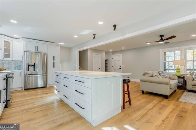 kitchen with a center island, backsplash, a kitchen breakfast bar, appliances with stainless steel finishes, and white cabinetry