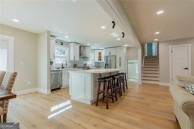 kitchen with white cabinetry, a center island, wall chimney exhaust hood, stainless steel appliances, and light hardwood / wood-style floors