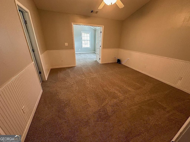 empty room featuring carpet floors, vaulted ceiling, ceiling fan, and wooden walls