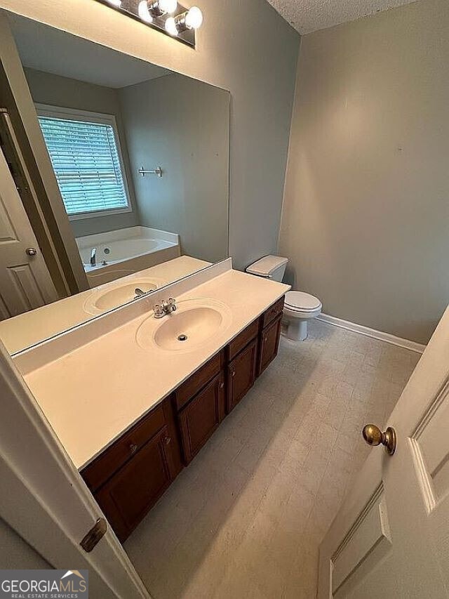 bathroom featuring a bathing tub, vanity, a textured ceiling, and toilet