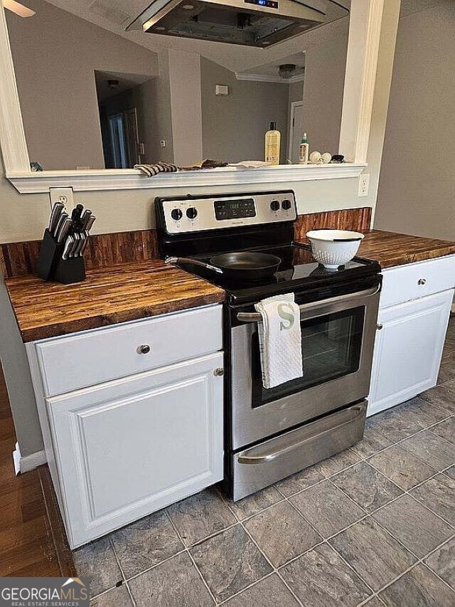 kitchen with stainless steel electric stove, butcher block countertops, white cabinets, and range hood