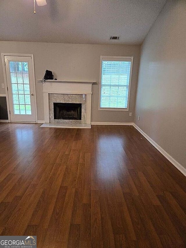 unfurnished living room featuring dark hardwood / wood-style flooring, a premium fireplace, plenty of natural light, and a textured ceiling