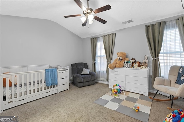 carpeted bedroom featuring lofted ceiling, multiple windows, ceiling fan, and a crib