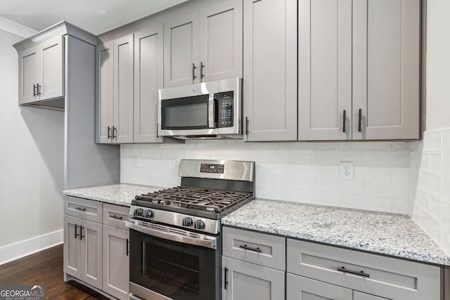 kitchen featuring decorative backsplash, light stone counters, stainless steel appliances, gray cabinets, and dark hardwood / wood-style floors