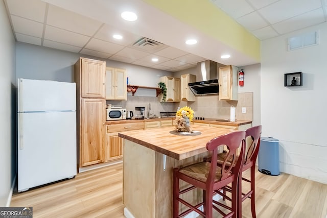 kitchen featuring wood counters, white appliances, light brown cabinetry, and wall chimney range hood