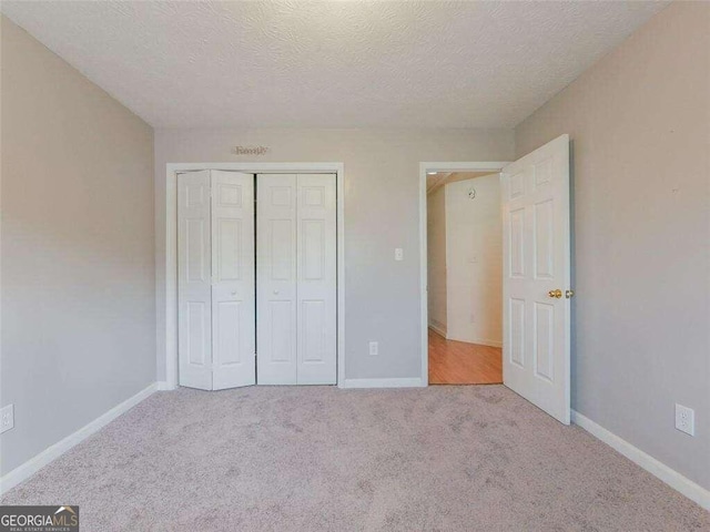 unfurnished bedroom featuring light colored carpet, a textured ceiling, and a closet