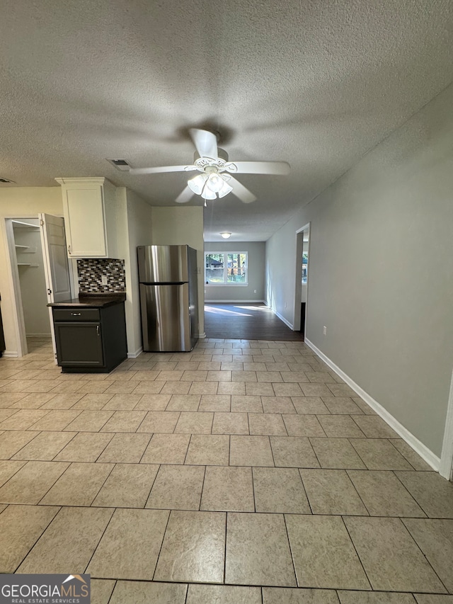 kitchen with backsplash, ceiling fan, a textured ceiling, white cabinetry, and stainless steel refrigerator