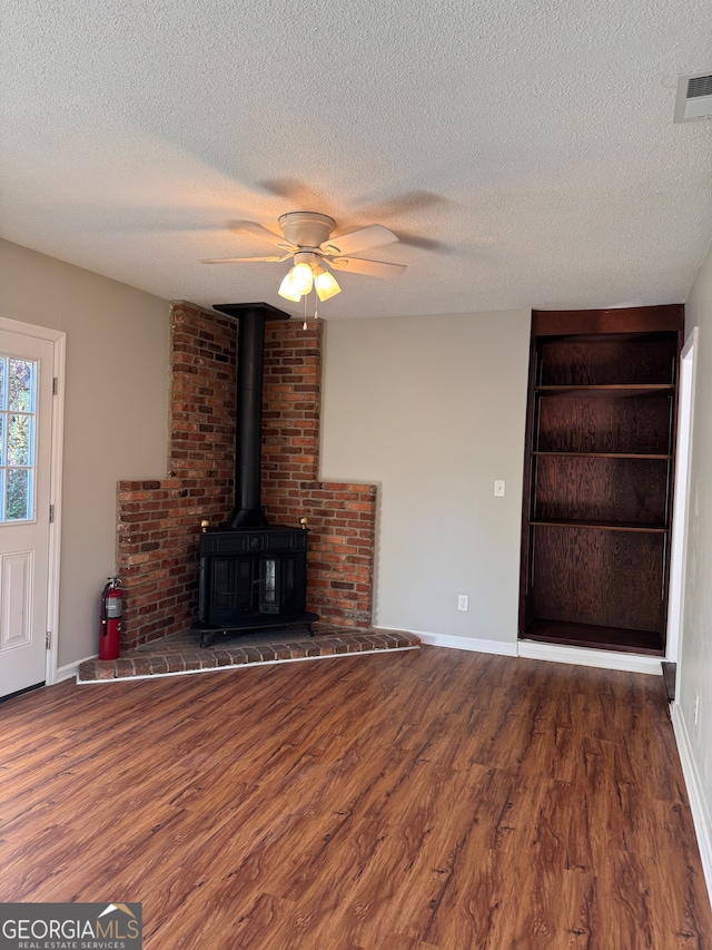 unfurnished living room featuring a textured ceiling, a wood stove, ceiling fan, and dark wood-type flooring