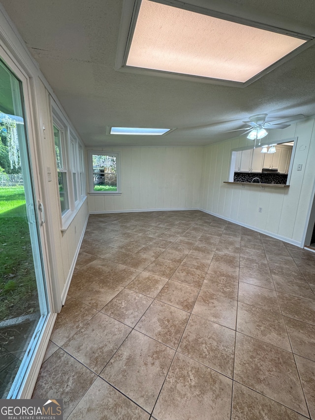 interior space with a skylight, ceiling fan, and a textured ceiling