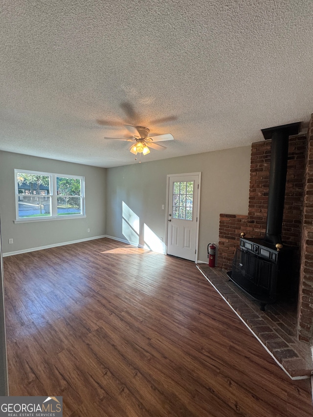 unfurnished living room with a wood stove, ceiling fan, dark wood-type flooring, and a textured ceiling