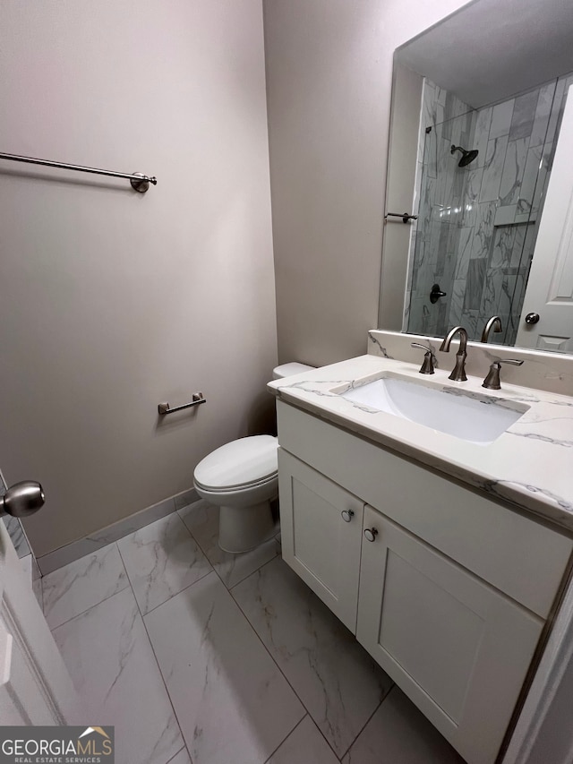 bathroom with a tile shower, vanity, and toilet