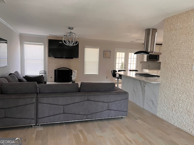 living room with french doors, a large fireplace, crown molding, a chandelier, and light hardwood / wood-style floors