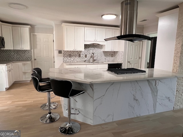 kitchen featuring island exhaust hood, kitchen peninsula, white cabinetry, and light stone countertops