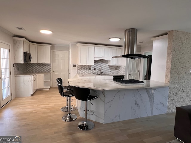 kitchen featuring island exhaust hood, a kitchen breakfast bar, sink, light hardwood / wood-style floors, and white cabinetry