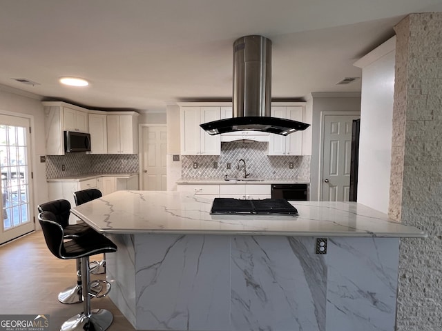 kitchen with a breakfast bar, white cabinets, black appliances, light stone counters, and island exhaust hood