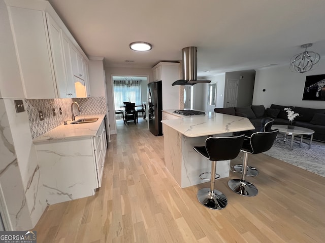 kitchen with white cabinetry, sink, light stone countertops, island exhaust hood, and black refrigerator