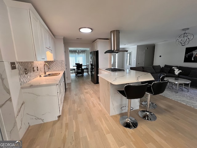 kitchen featuring black fridge, island range hood, sink, light hardwood / wood-style flooring, and white cabinets