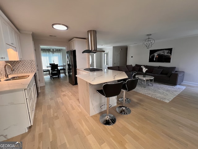 kitchen with island exhaust hood, black refrigerator, sink, a chandelier, and white cabinetry