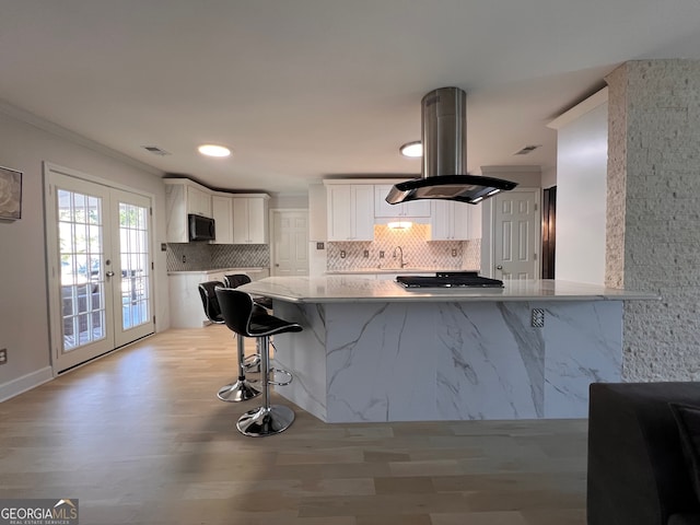 kitchen with kitchen peninsula, white cabinetry, french doors, and island range hood