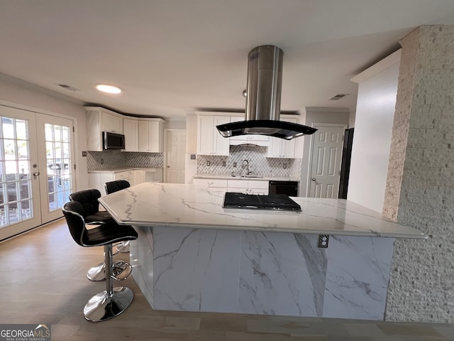 kitchen featuring french doors, white cabinets, light stone counters, a kitchen bar, and kitchen peninsula